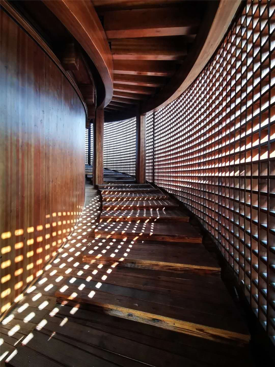 A curved wooden lattice corridor, sun falling through the slats in stripes