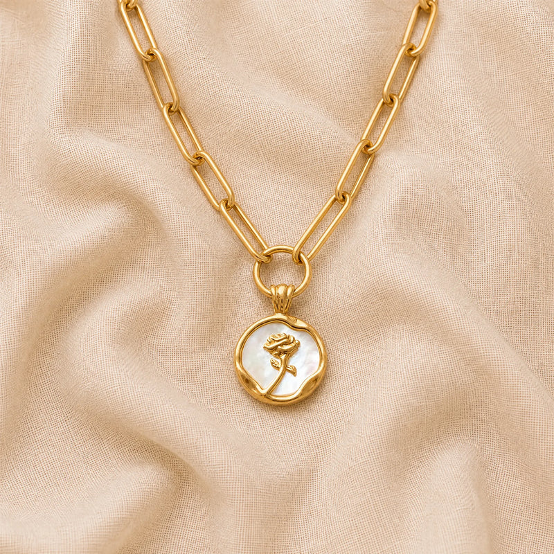 Gold paperclip chain necklace with a mother of pearl rose pendant on a beige fabric background