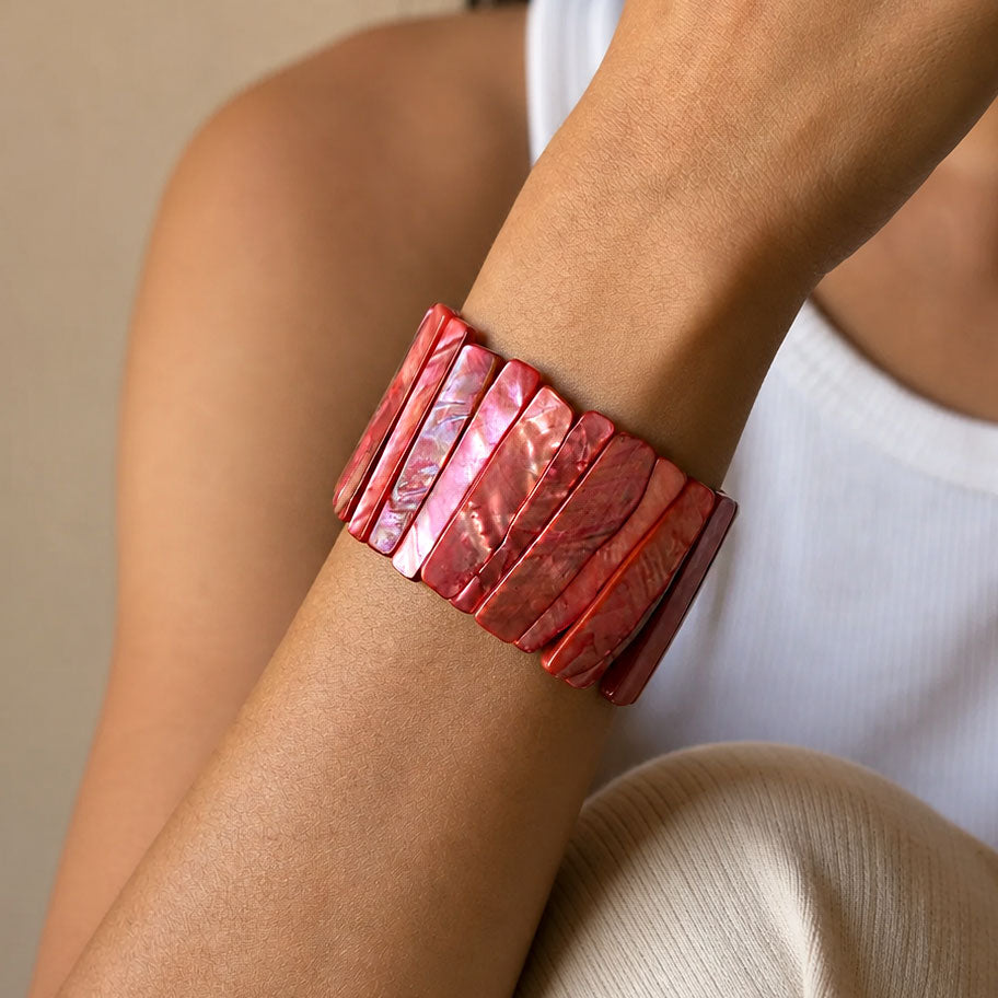 A close-up of a person's wrist wearing a wide, chunky cuff bracelet made of polished rectangular pinkish-red shell pieces.
