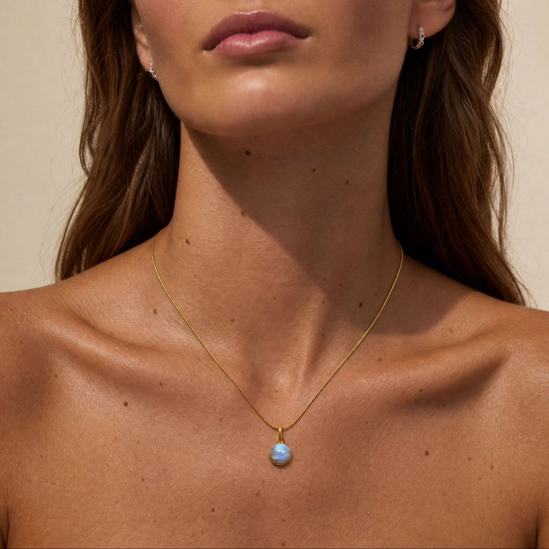 Close-up of a woman wearing a gold necklace with a blue pendant against a neutral background