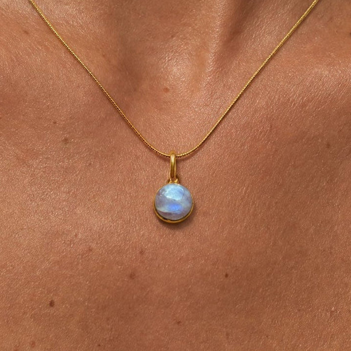 Close-up of a woman wearing a gold necklace with a blue pendant against a neutral background