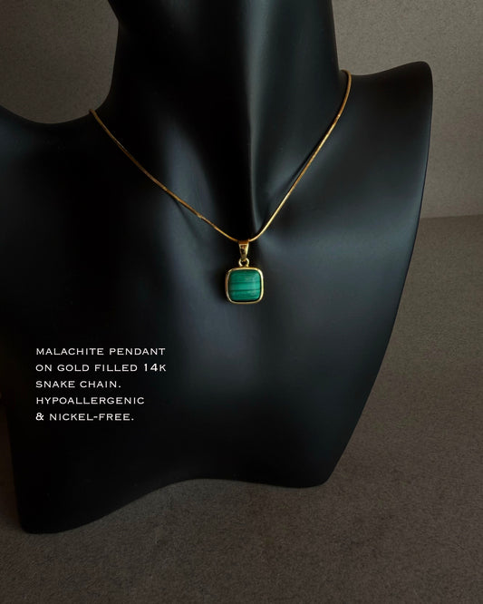Necklace with malachite pendant on gold chain displayed on a black mannequin bust.