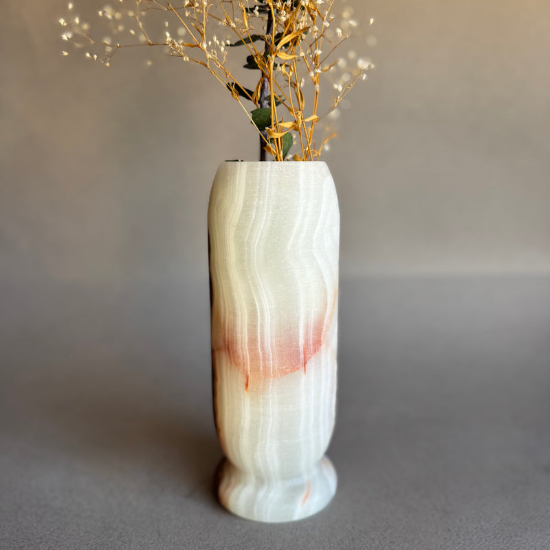 Marble-patterned pink white onyx vase with dried plants on a neutral background
