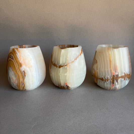 Three onyx stone cups with marbled patterns on a gray background