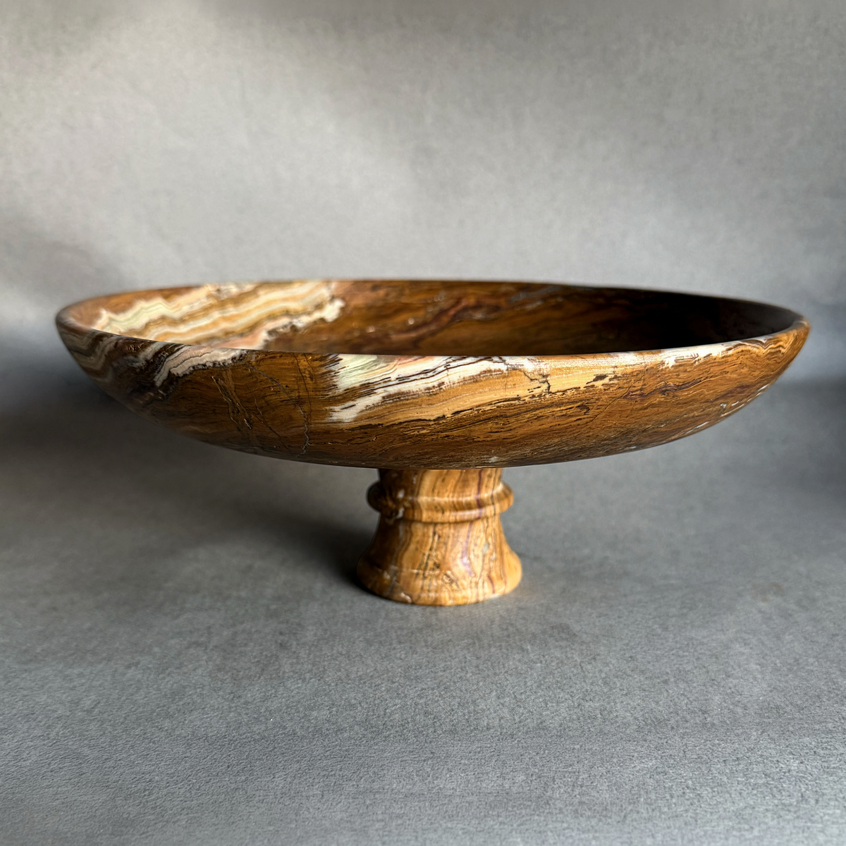 Hand-carved natural onyx pedestal bowl in brown, sienna, and amber tones on a neutral background