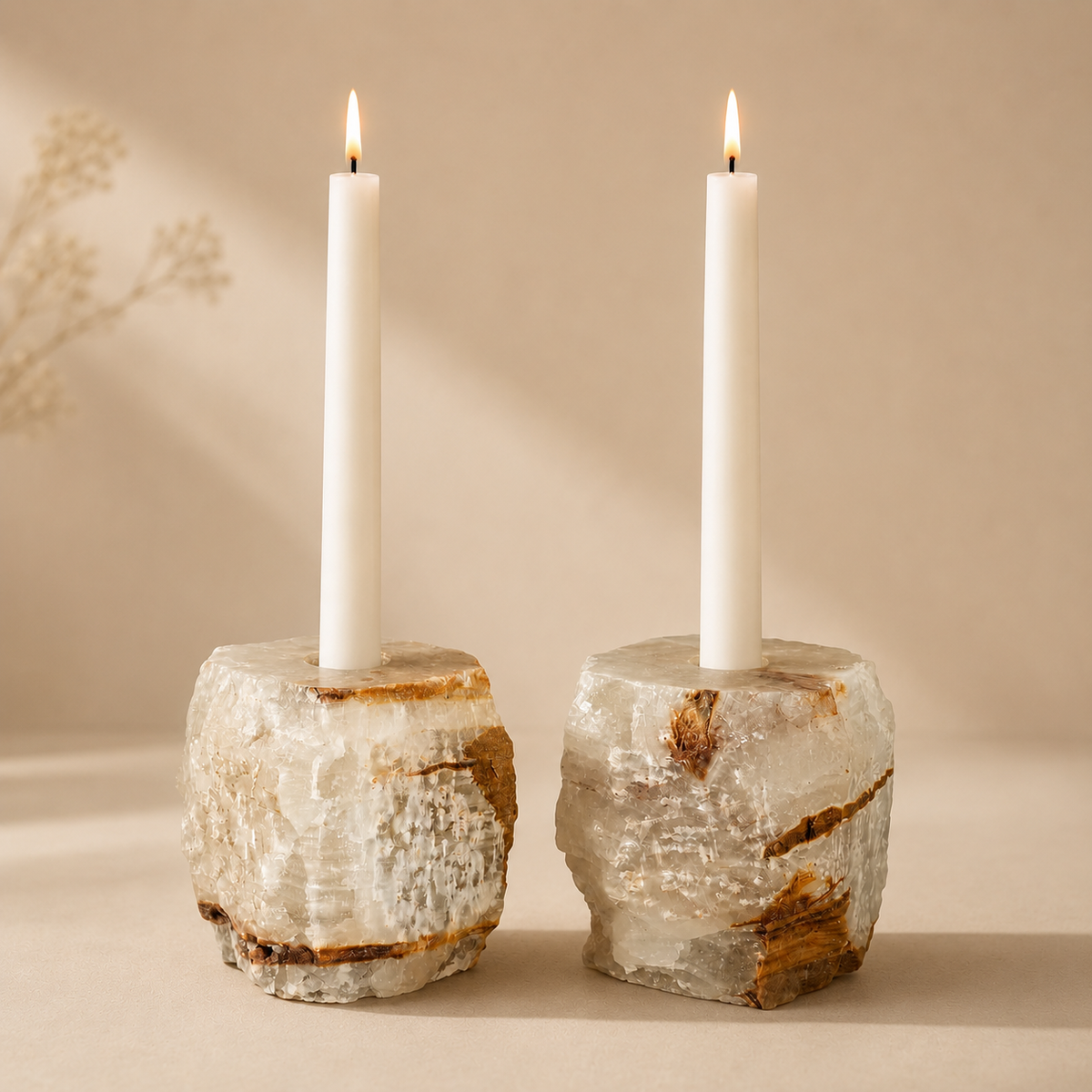 Two white taper candles standing in rough, natural stone holders with a warm beige background.