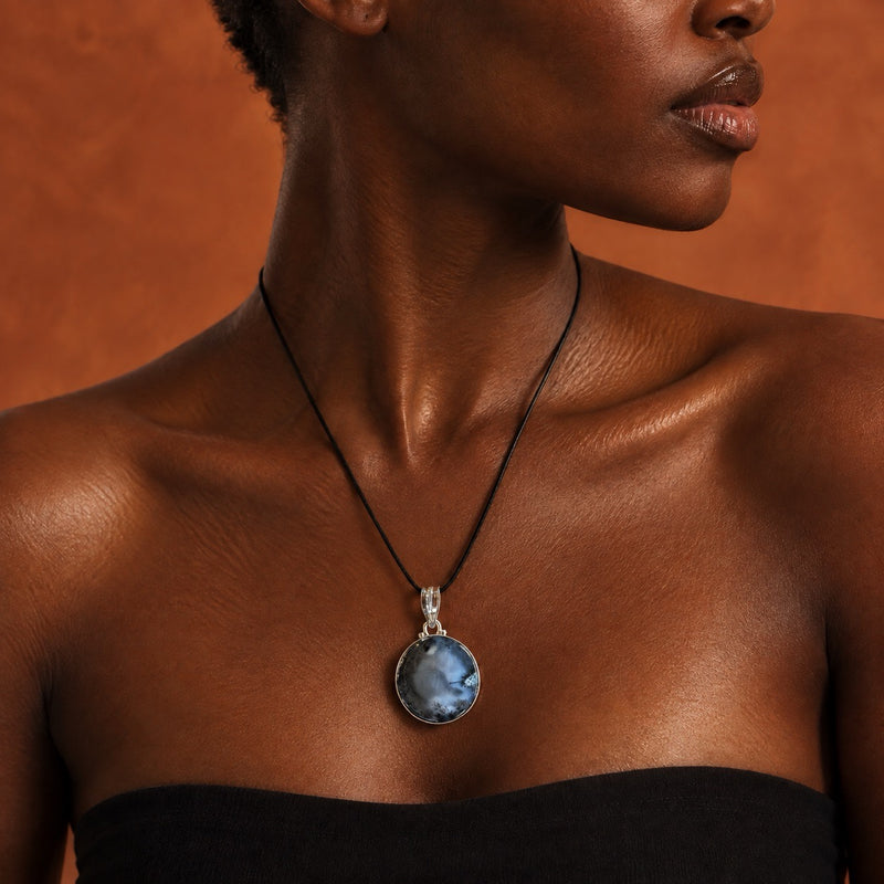 Dendritic opal pendant on a black cord worn at the collarbone, pale blue stone with black inclusions