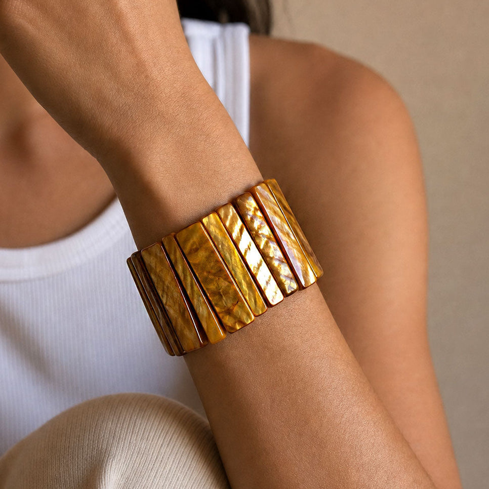 A close-up of a person's wrist wearing a wide, chunky gold-toned cuff bracelet made of textured rectangular segments.