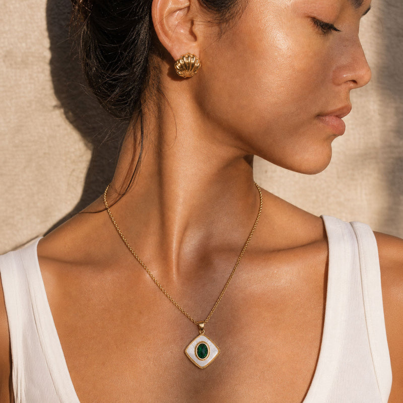 Close-up of a woman wearing a gold necklace with a green pendant against a neutral background