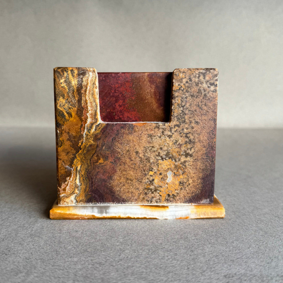 SAÉA onyx coaster holder in burnt sienna and rust, front view showing swirled amber-gold veining on a cream base.