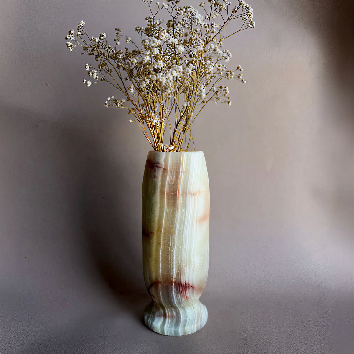 Decorative green light onyx vase with a natural stone pattern containing dried flowers on a plain background