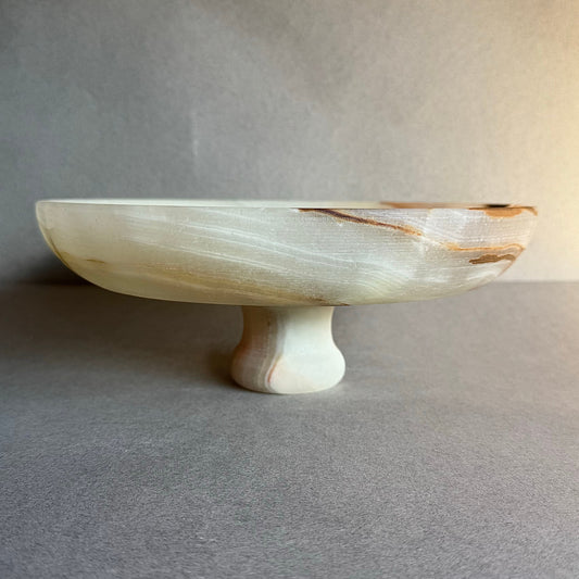 Hand-carved stone pedestal bowl, ivory and beige tones with rust accents.