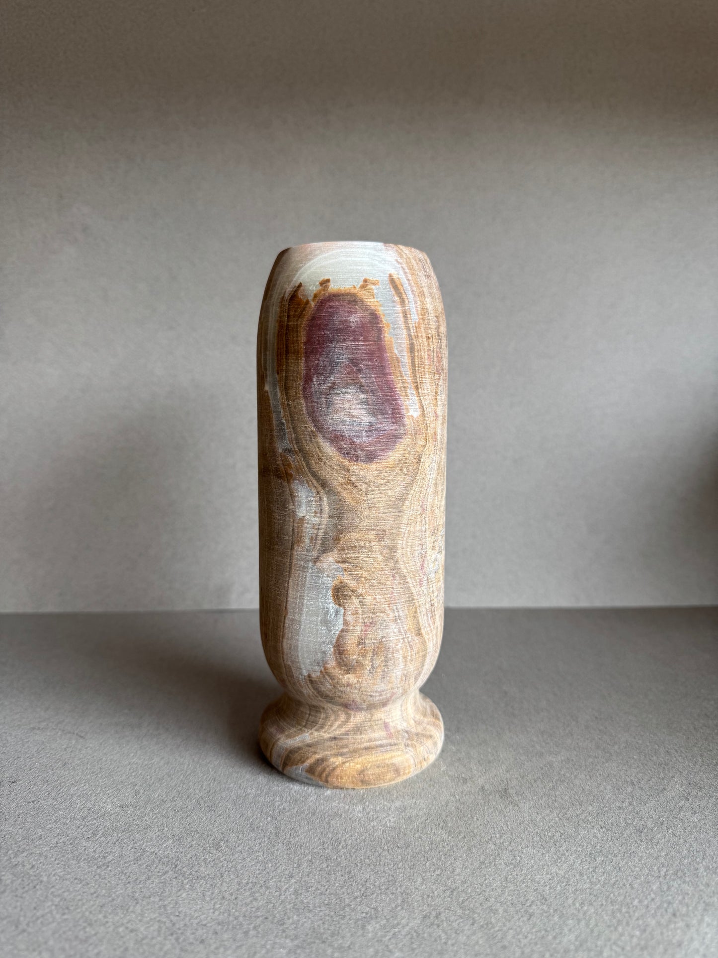 Tall onyx vase with dramatic rose-toned mineral bloom, hand-carved with a pedestal base and natural matte finish.
