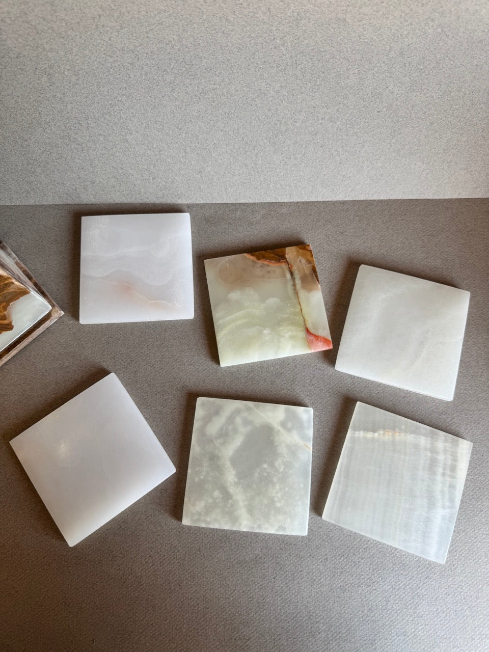 Flat lay of six square onyx coasters in cream, sage, and caramel tones with varied natural patterns