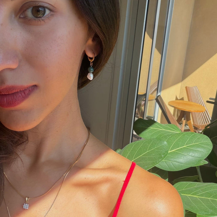 Woman wearing a red top with a blurred indoor background with gold filled huggie earrings with freshwater pearl and jade