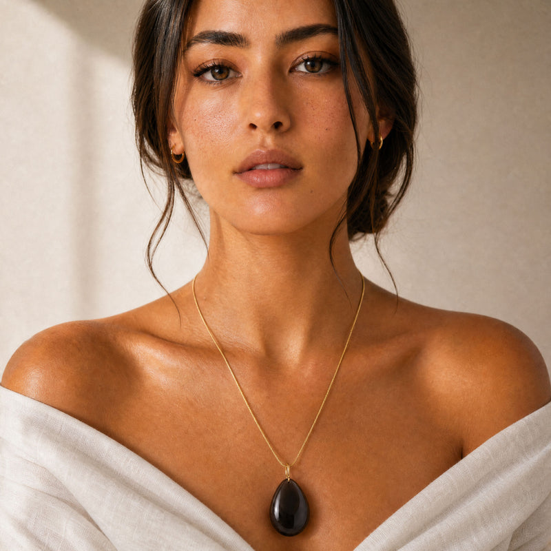 Woman wearing a gold necklace with a dark OBSIDIAN large pendant against a neutral background