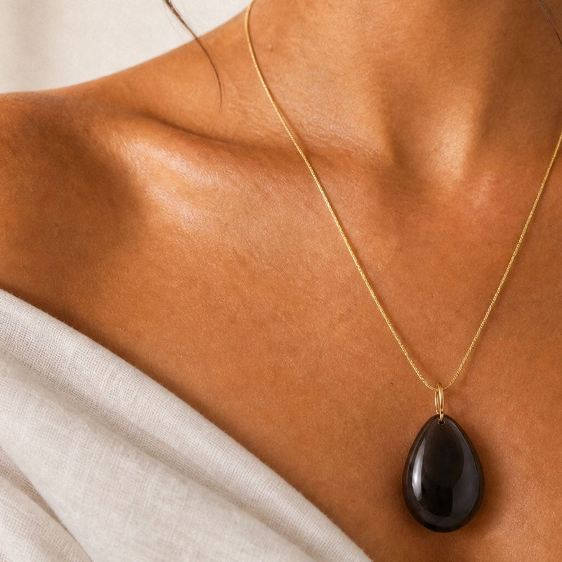 Woman wearing a gold necklace with a dark OBSIDIAN large pendant against a neutral background