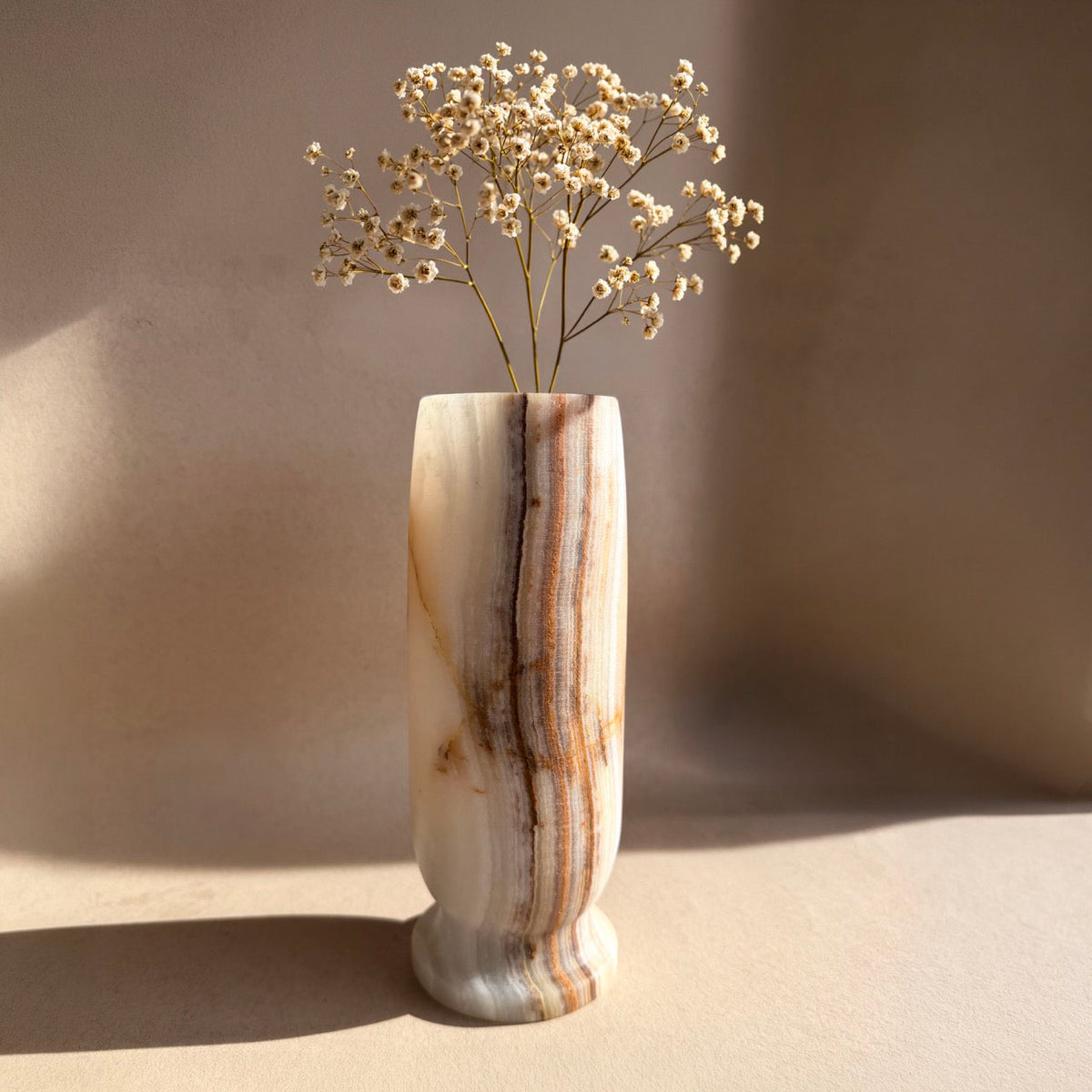 Hand-carved onyx Origin Vase in ivory and caramel with soft rust banding, lit against a pale neutral backdrop.