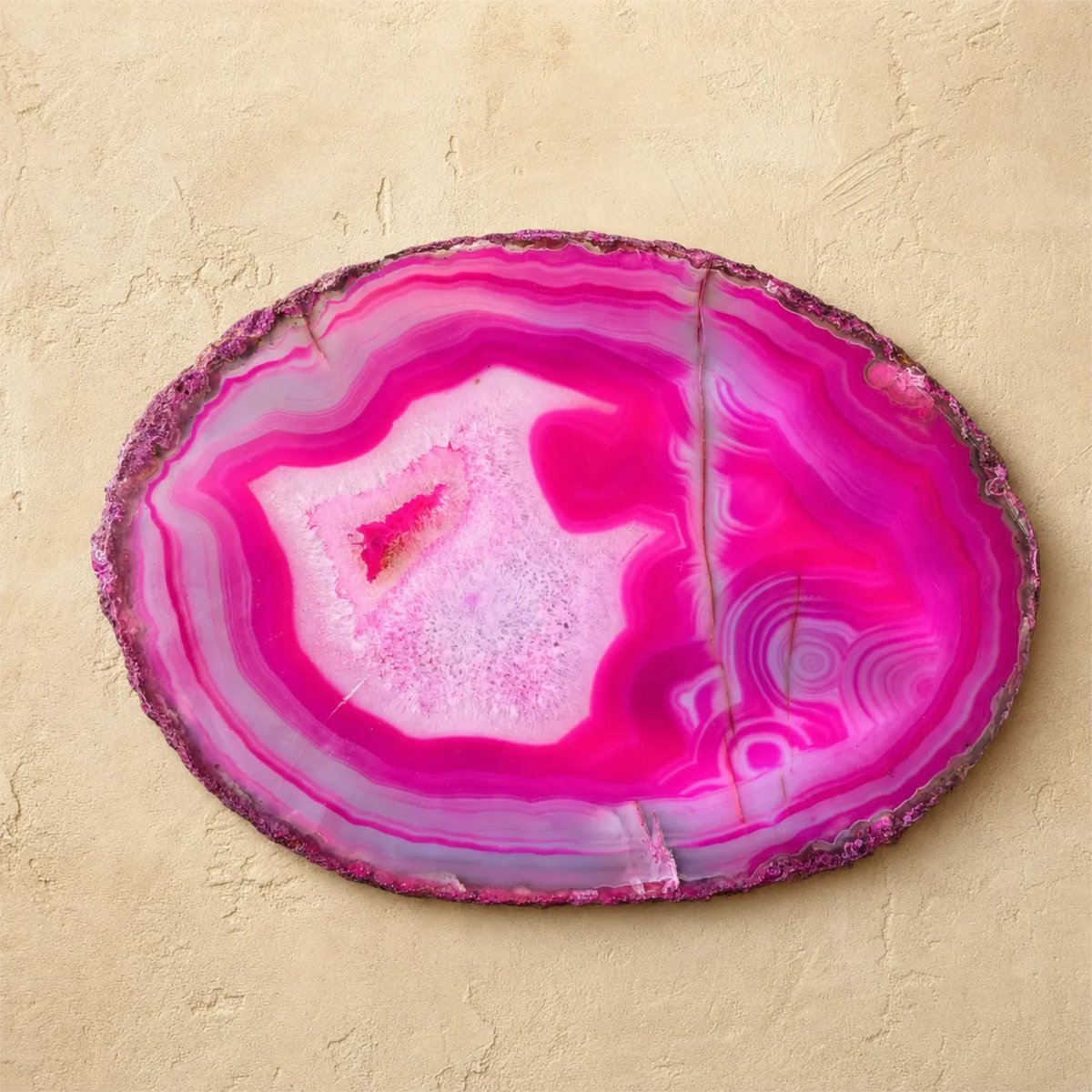 A polished oval agate slice wall decor piece with vibrant magenta, pink, and purple banded patterns, displayed on a textured beige plaster background.