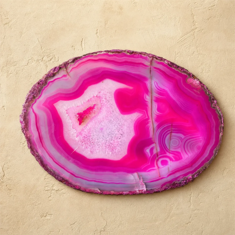 A polished oval agate slice wall decor piece with vibrant magenta, pink, and purple banded patterns, displayed on a textured beige plaster background.