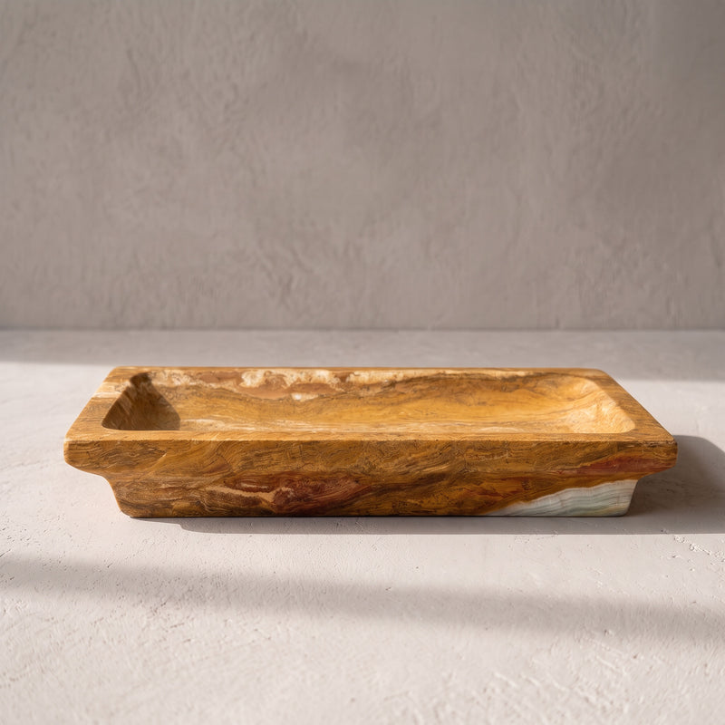 Low side view of the dark tobacco onyx catchall tray, its hand-carved rim and honey banding on pale plaster