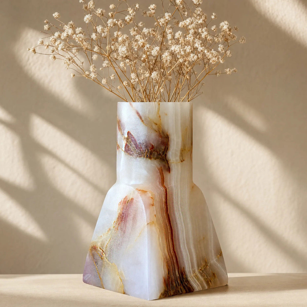 Geometric white onyx vase with vertical rust-red and amber veining, square base to round neck, in window light