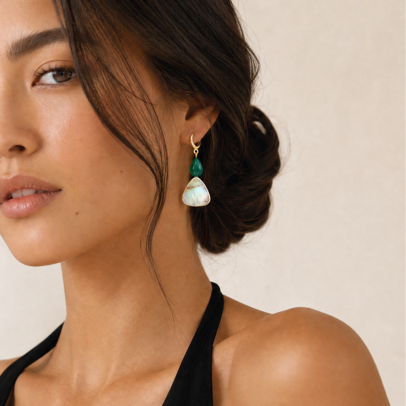 Woman wearing a black top and green malachite and white mother of pearl earrings against a beige background