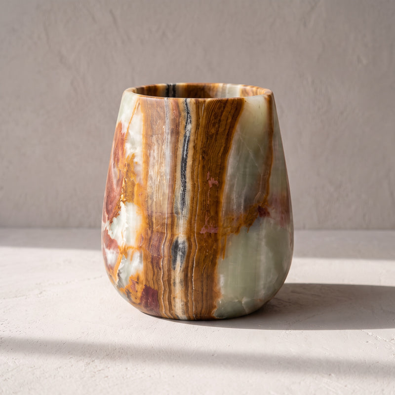 Saffron, sienna and cream banded onyx curved vessel with a dry-honed matte finish, on pale plaster in raking sun