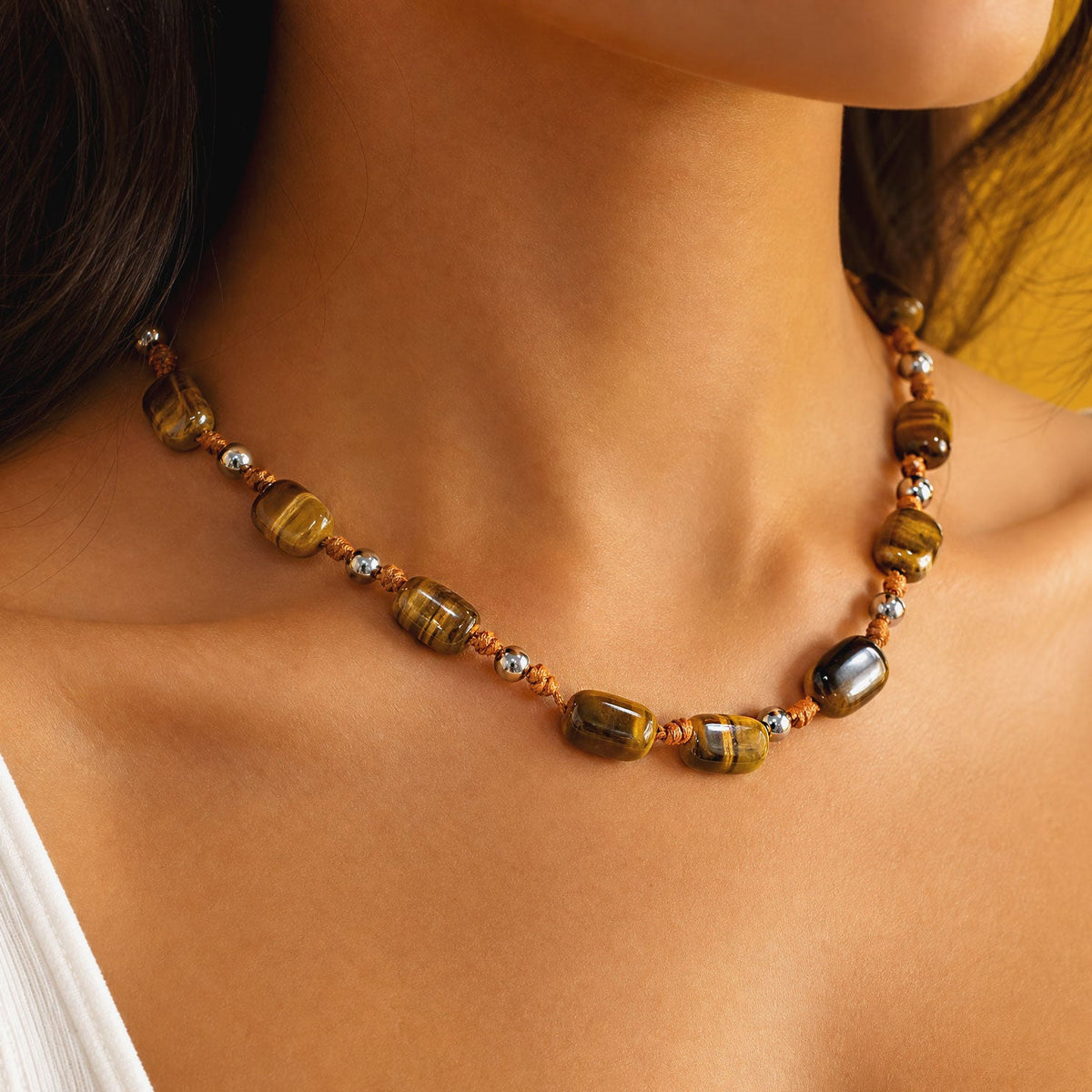 Close view of the tiger's eye beaded strand along the collarbone, showing graduated honey-gold and darker banded stones with polished silver-tone spacers.