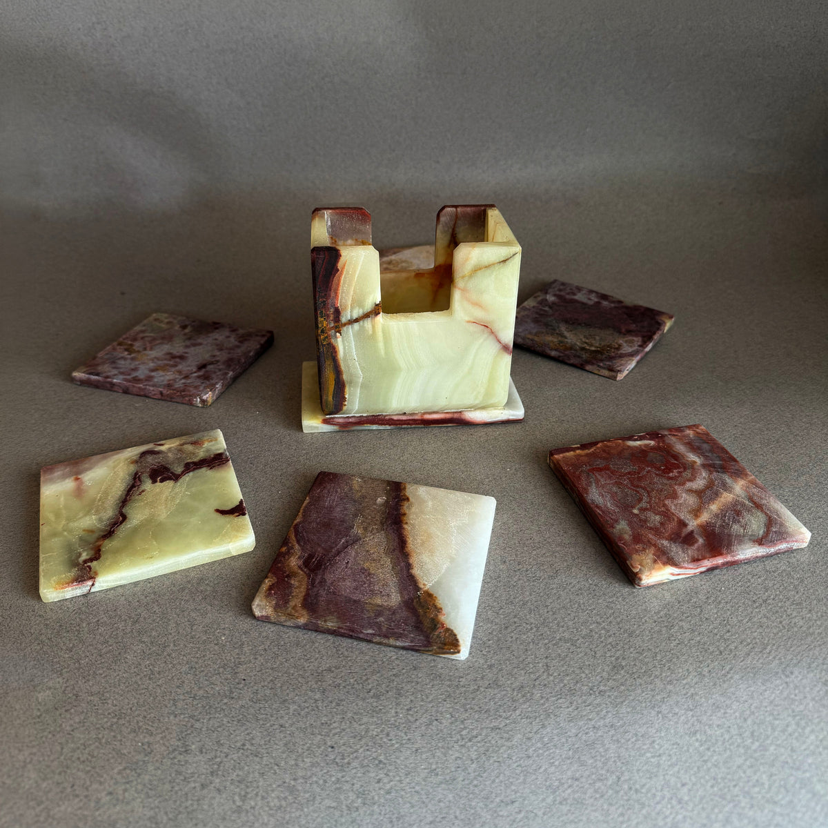 Set of six square onyx coasters in jade, sand and clay tones fanned around their matching holder