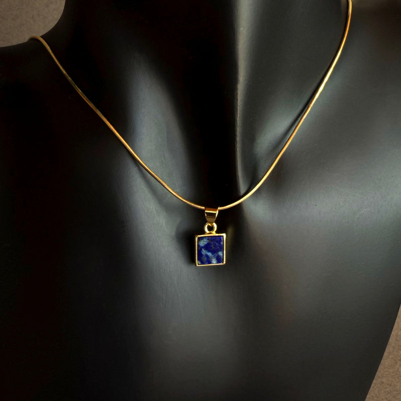 Gold snake chain necklace with a blue lapis lazuli pendant on a dark background