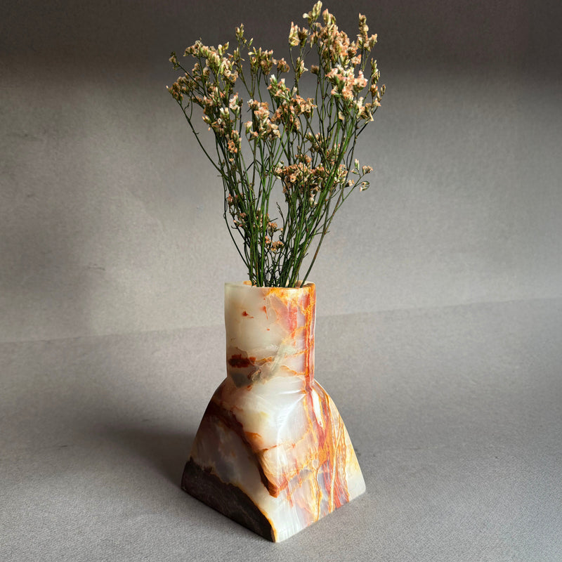 Blush and amber onyx vase with dried florals on a gray surface against a plain gray wall