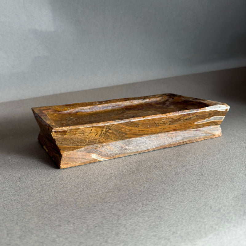 Hand-carved brown onyx catchall tray with warm amber and honey veining, raw natural stone vanity tray styled with watch and perfume bottle on neutral background