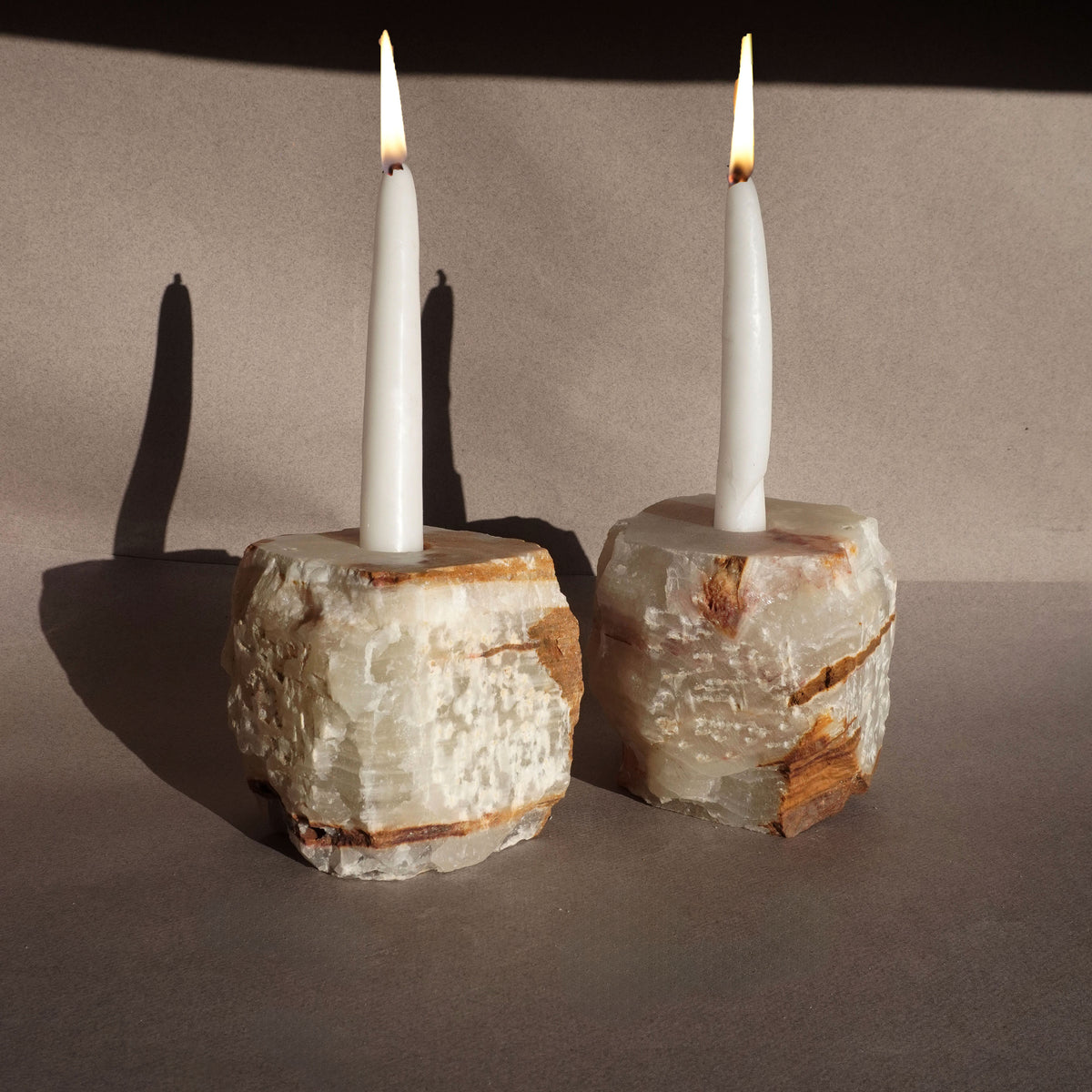 Hand-carved natural onyx taper candle holders in soft cream and honey tones with lit white candles on neutral backdrop