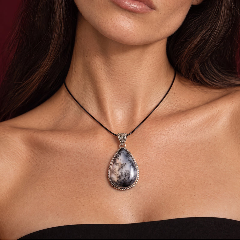 Storm-gray and cloud-white dendritic opal teardrop pendant in a rope-edged sterling silver bezel on a short black cord, worn at the collarbone
