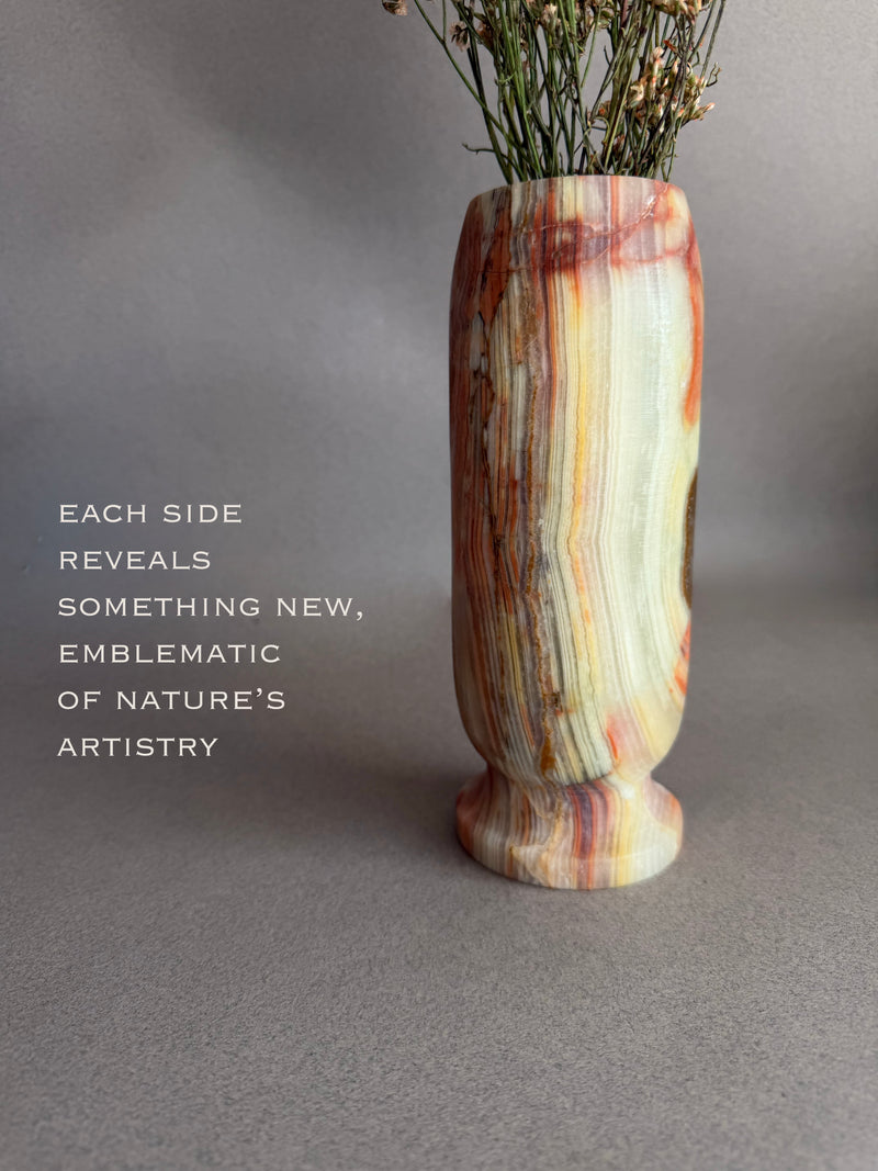 Marble-patterned red green rust amber onyx natural stone vase with dried flowers on a gray background