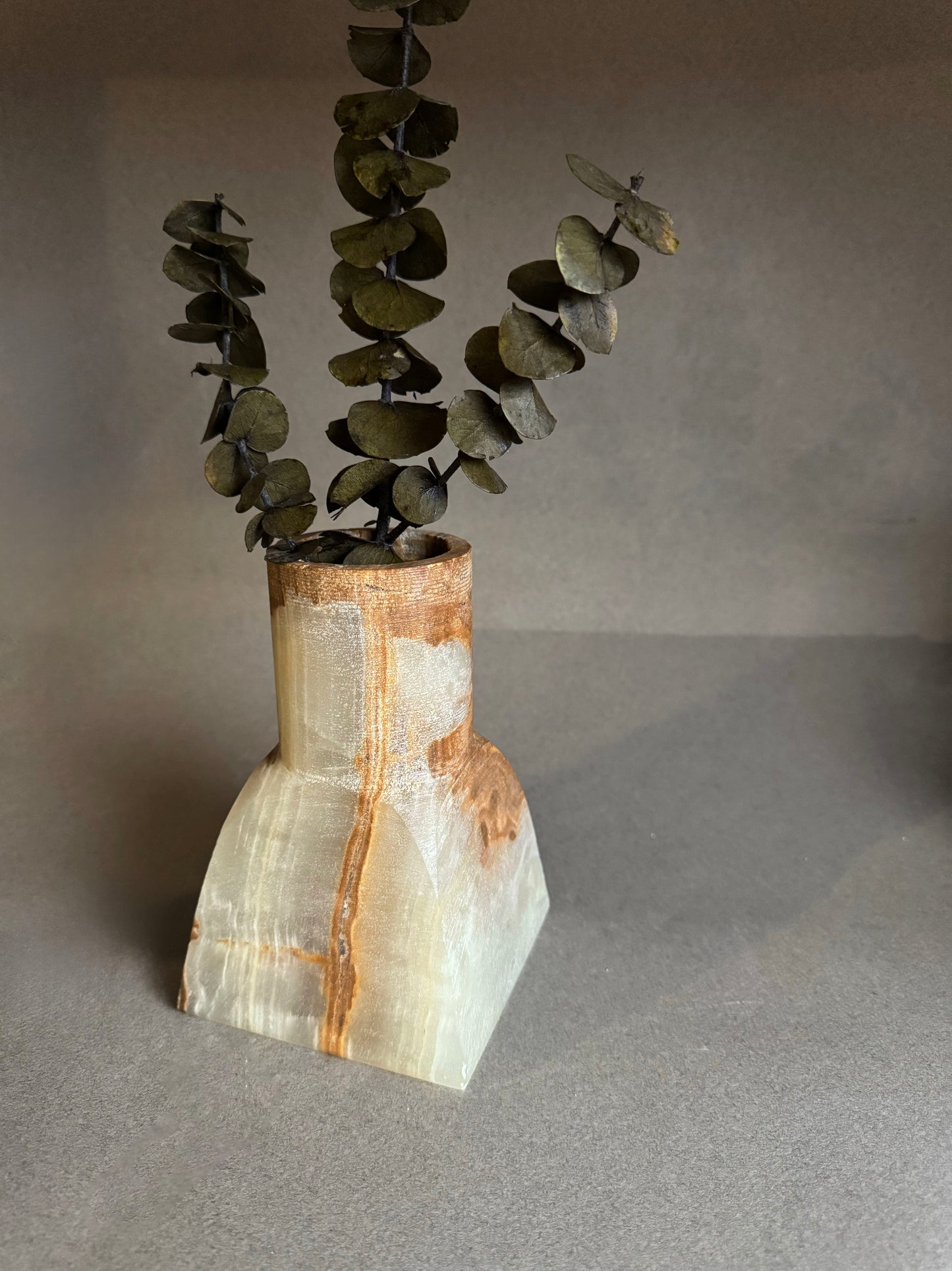 Vase with a natural stone design holding eucalyptus leaves on a gray background