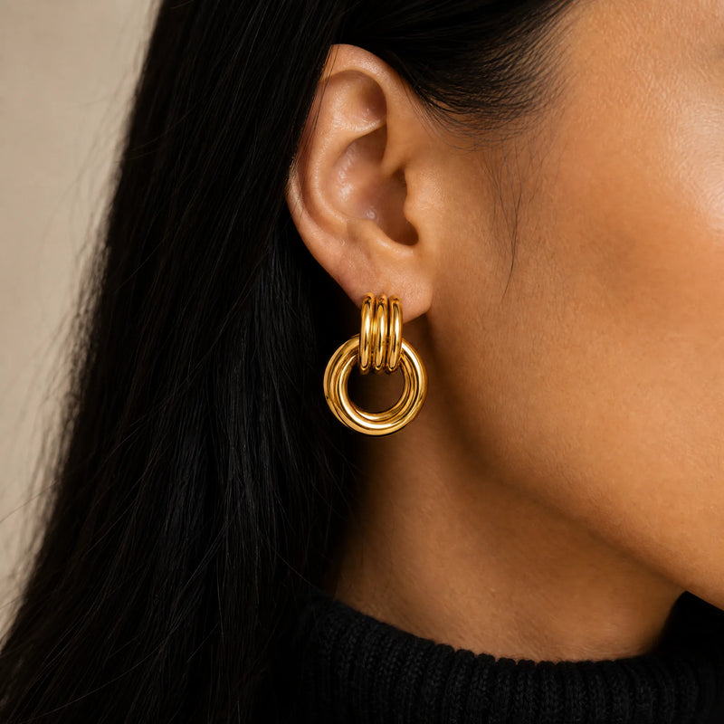Close-up of a person wearing a gold knot earring with a neutral background. Heaven mayhem knot earring dupe