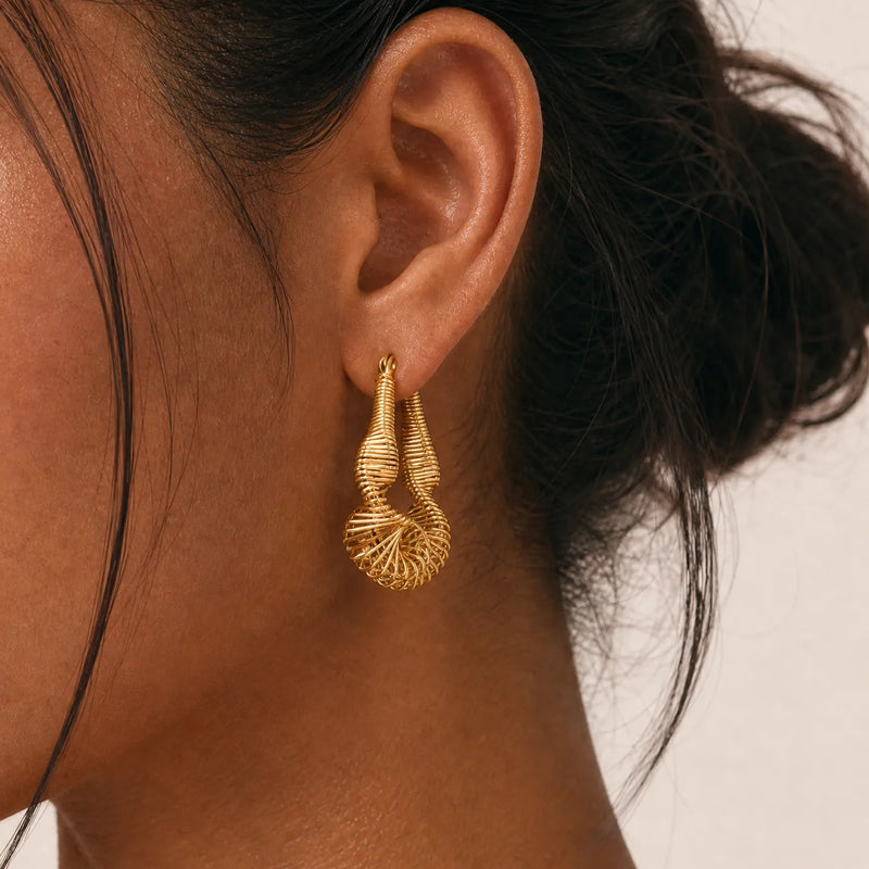 Close-up of a woman wearing gold earrings with a neutral background