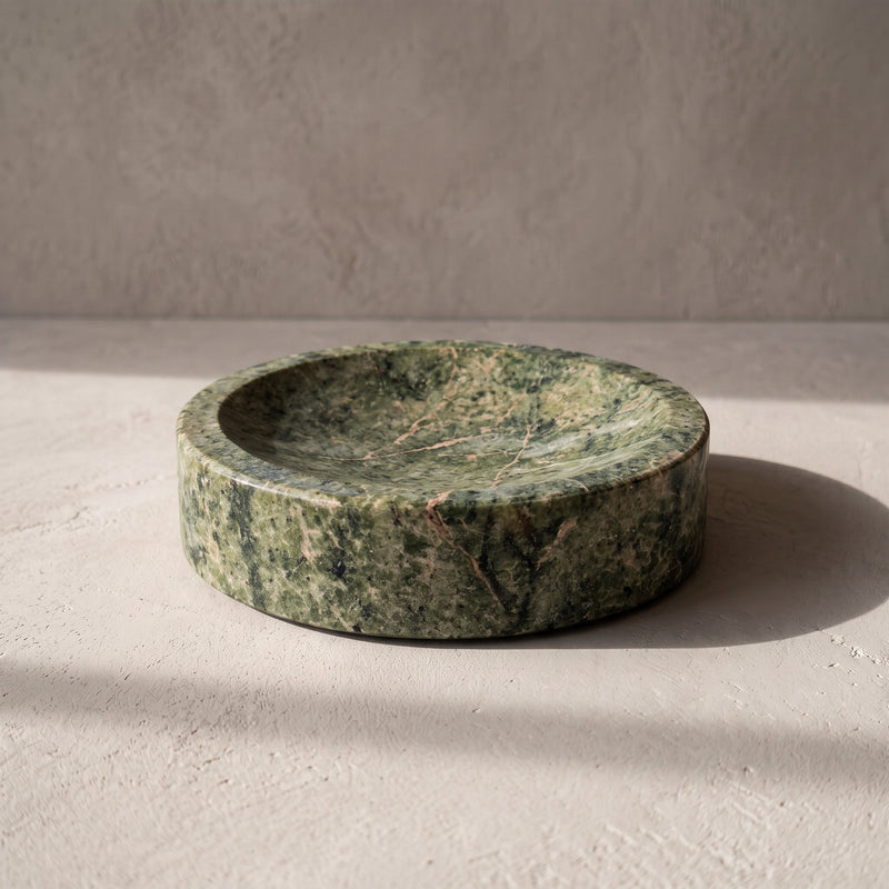Three-quarter view of the fern green marble catchall bowl, a small rust bloom at the upper rim