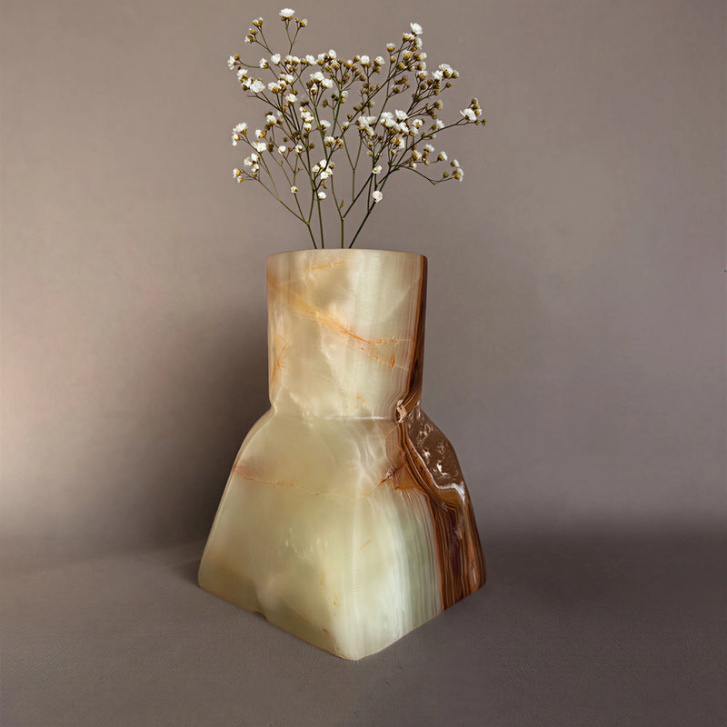 Decorative green onyx vase with a natural stone pattern containing small white flowers on a plain background sculptural home decor
