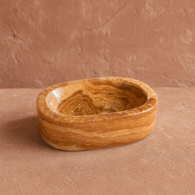 Honey and caramel polished onyx oval catchall bowl, three-quarter view against a terracotta ground