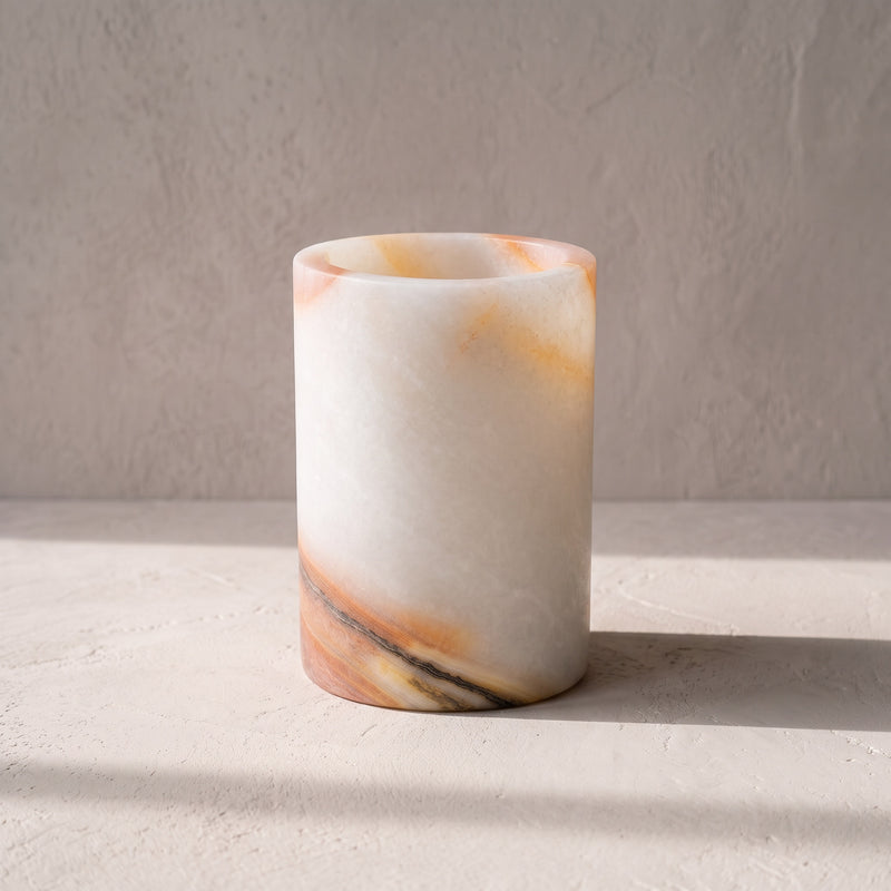 Ivory onyx flat vessel straight on, coral veining at the rim and a charcoal and coral seam across the base, on a pale plaster surface.
