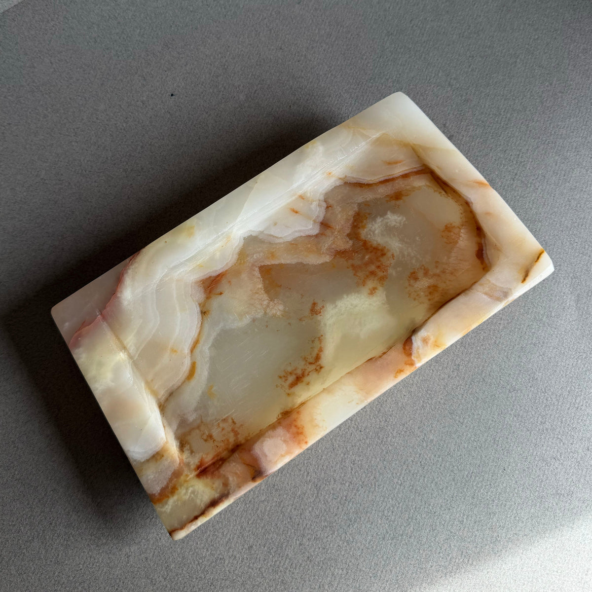 Rectangular peach honey onyx white stone tray with marbled pattern on a gray surface