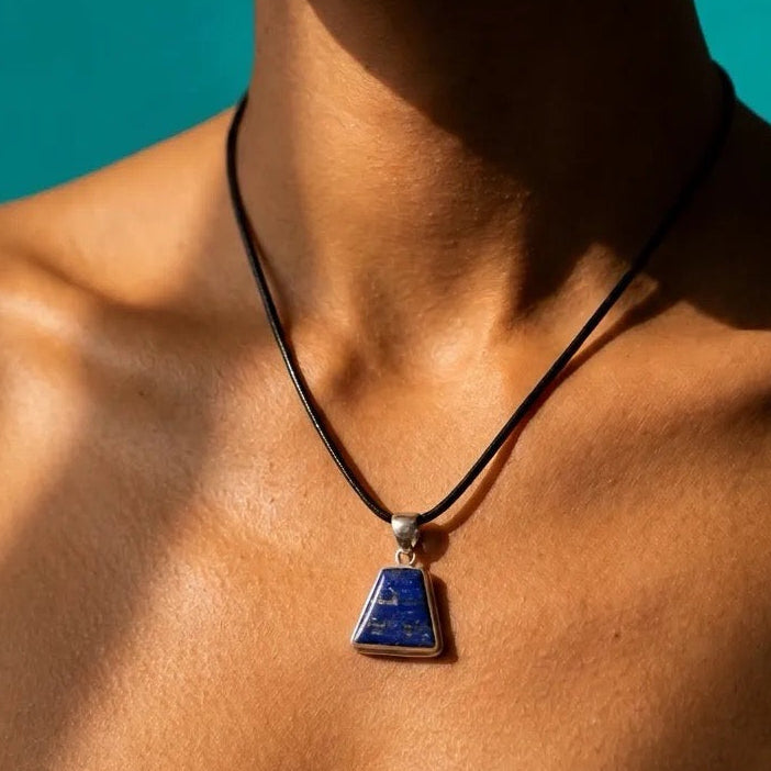 A close-up lifestyle shot of a model wearing a black cord necklace with a triangular blue and white lapis lazuli patterned pendant.