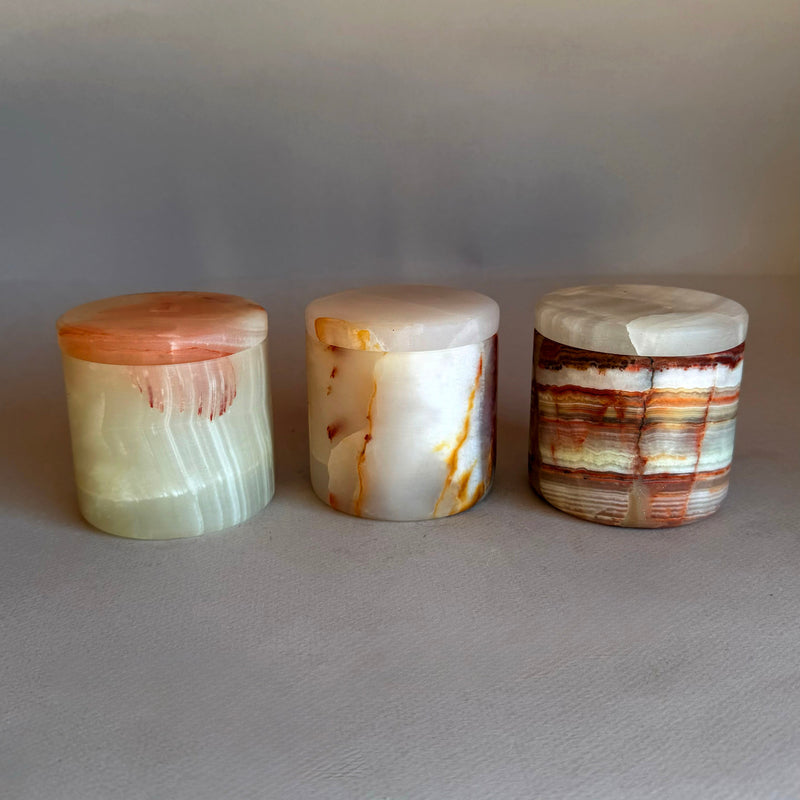 Three petite lidded onyx keepsake jars side by side in cream, ivory and banded rust tones