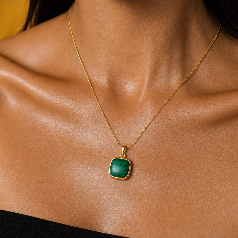 A gold chain necklace with a square green malachite pendant, worn by a model.