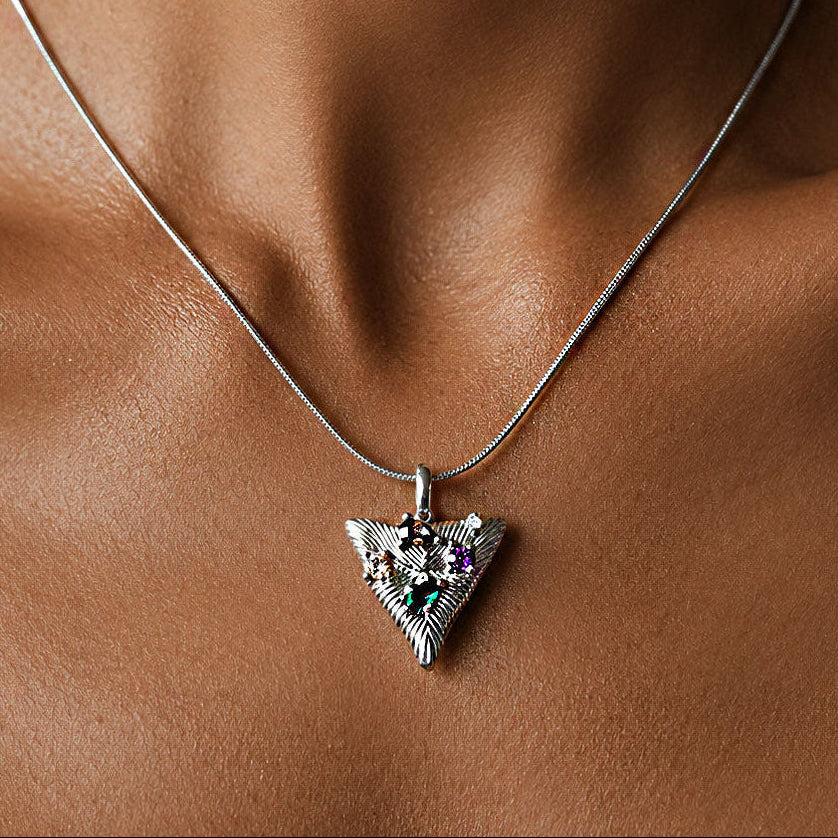 Silver arrowhead pendant necklace with olive, amethyst, emerald, and clear cubic zirconia stones resting against the collarbone on a fine snake chain.