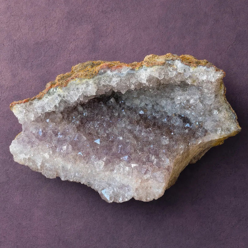 Natural amethyst geode standing upright, ochre matrix rind on the outside with a band of pale crystal along the base.