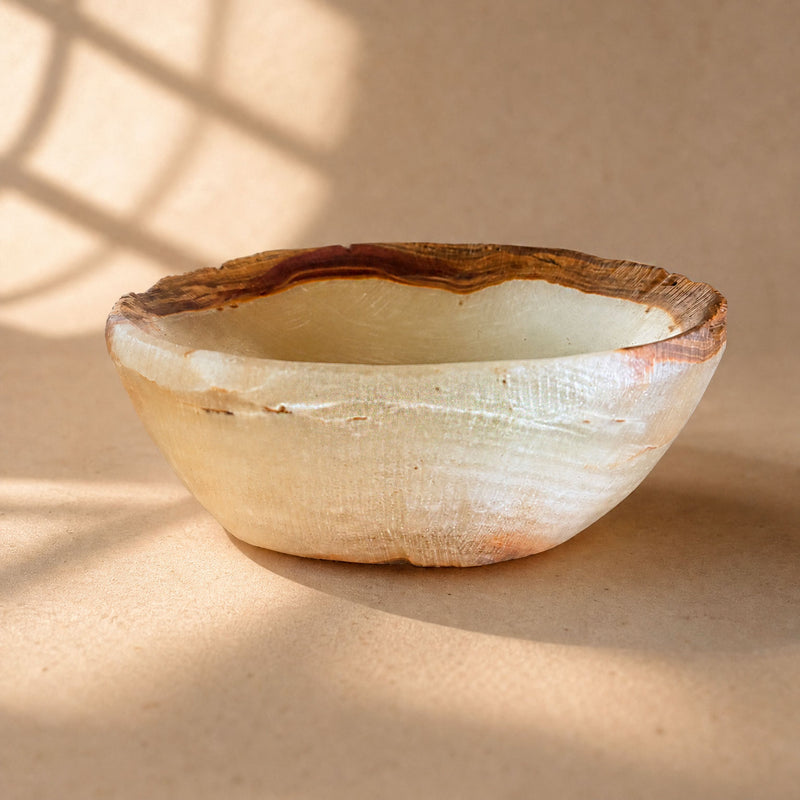 Bone and burgundy raw edge onyx bowl, honey-brown striated rim with burgundy vein, on sunlit surface